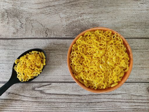 An overhead shot of raw pasta in a bowl and a big spoon on a wooden surface