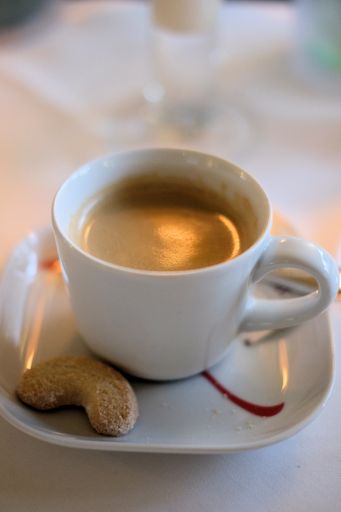 A vertical shot of a delicious cup of coffee and a cookie on the plate with a blurred background