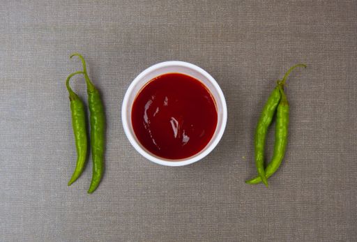 A top view of green chili peppers and a bowl of ketchup on a grey surface