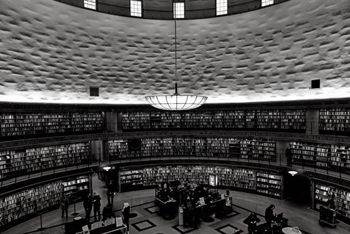 An atmospheric black and white image of a large library in Stockholm, featuring a group of people gathered amongst the shelves
