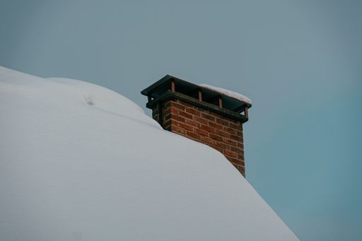 A low angle shot of a house covered with snow with red brick chimney