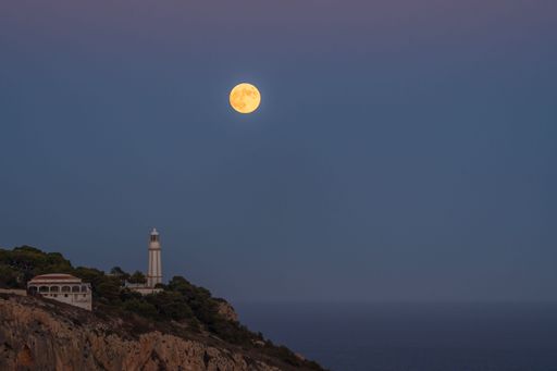 A stunning night scene featuring the moon setting near the peak of a mountainous landscape