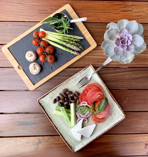 An overhead shot of salad with beans and cheese on a plate near a wooden tray with vegetable on it near a rose