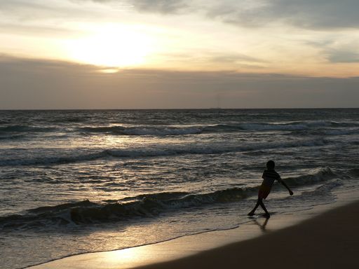 A young boy on the sandy Hikkaduwa beach playing with the water  during the sunset