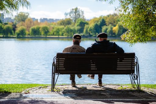 Two young Caucasian adult men sitting on a wooden bench outdoors enjoying the view of a tranquil lake