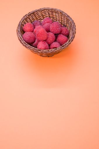 A vertical shot of a small basket with fresh raspberries isolated on a light-colored background