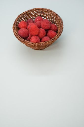 A vertical shot of a small basket with fresh raspberries isolated on a white background