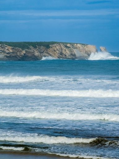 A vibrant seascape with a rocky coastline illuminated by sunlight and crashing waves against the shore
