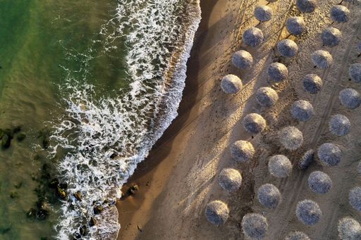 An overhead shot of beautiful beach waves hitting the shore with beach parasols on a sunny day