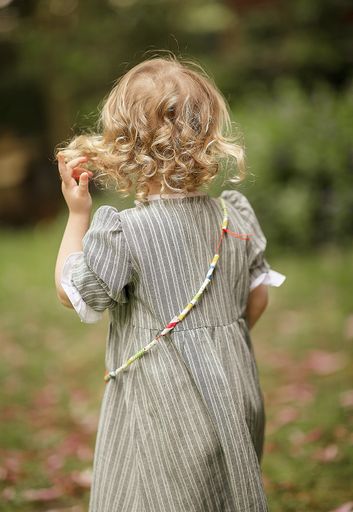 A vertical shot of a small Caucasian girl in a long dress with her back  outdoors