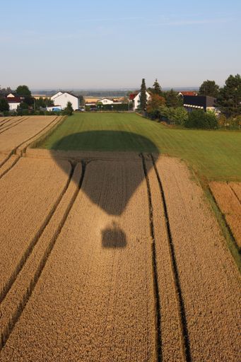 A vertical shot of the shadow of a big hot-air balloon over a field of hay and grass
