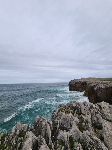 A scenic view of a blue ocean and rock cliffs in Asturias, Spain on a blue sky background