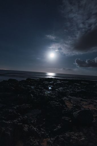 A vertical shot of the white moon shining in the horizon at the rocky beach