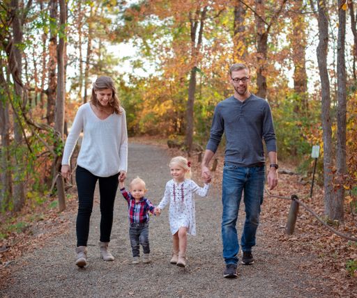 An adorable family of four holding hands and walking on a road that goes through a forest in Texas