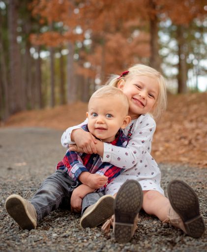 A shallow focus shot of two little blonde siblings hugging and sitting on the ground in a forest in Texas