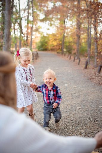 A shallow focus shot of little blonde kids holding hands and running to their mother in the forest