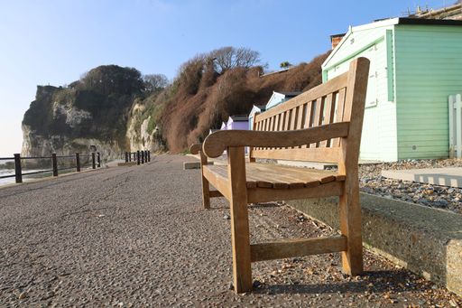 A wooden bench is situated in front of a vibrant green building with a breathtaking view of the ocean