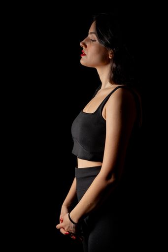A side view of an elegant brunette caucasian woman in a black outfit posing against a dark background
