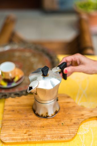 A woman's hand holding metal pot and pouring coffee into a cup