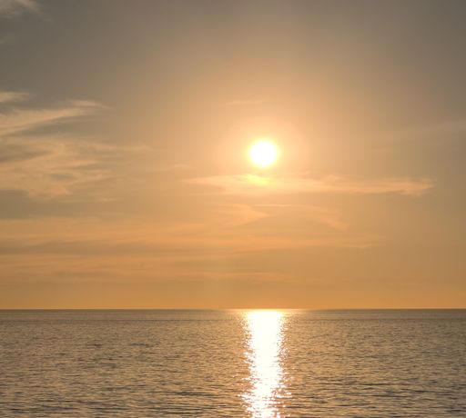 A sailboat is depicted sailing across the horizon as the sun rises over the ocean