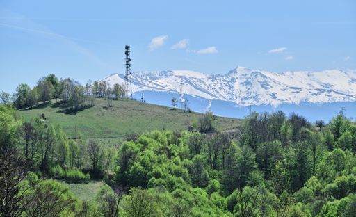 A landscape of greenery surrounded by rocky mountains covered in the snow under the sunlight