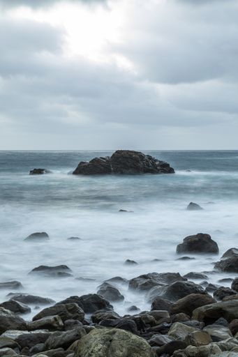 A vertical shot of a rocky shore with a flowing sea