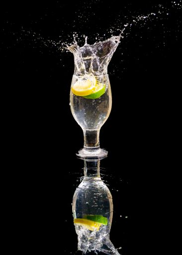 A vertical shot of  lemon slices splashing into glass water on isolated black background