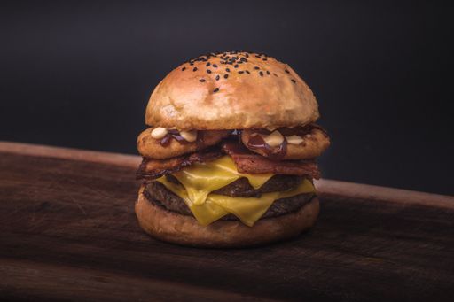 A closeup of a fresh double cheeseburger with onion rings and sauce on a wooden board