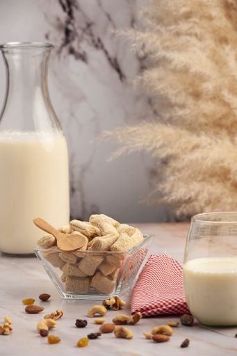 A vertical closeup shot of a gourmet bowl of cereal and a glass jar of milk on a kitchen table