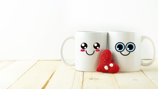 A closeup shot of two white cute mugs with an amigurumi heart pattern on white background