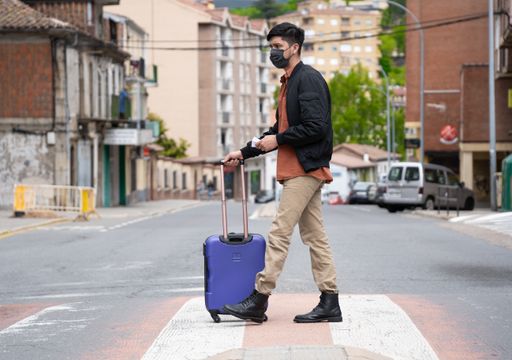A closeup of a person in a facial mask crossing the street with luggage - a new normal concept