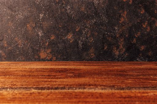 A closeup of a wooden surface with space for text against a dark textured wall