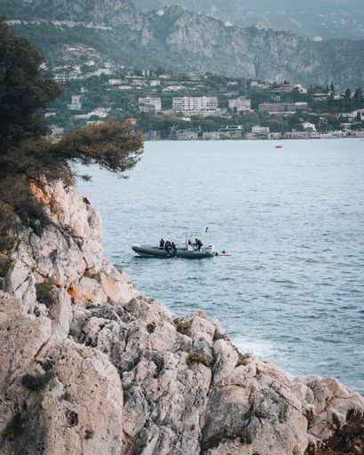 A vessel sailing on tranquil water surrounded by majestic mountains and jagged rocks in Nice, France