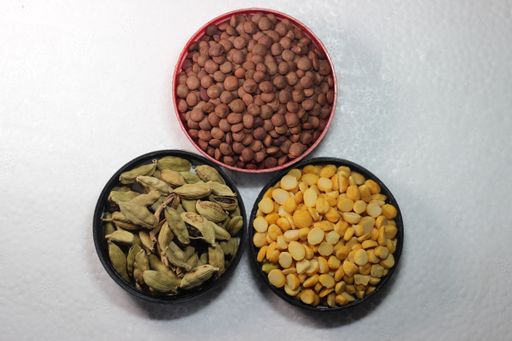 A top view of bowls of cardamom, dried dal, and lentil on a white surface