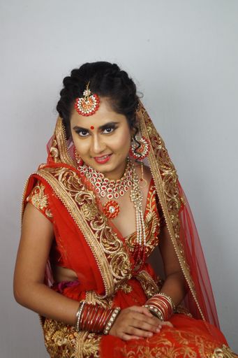 A beautiful Indian woman in a traditional red sari dress posing against a white wall