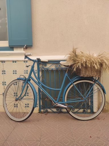 An aesthetically pleasing view of a blue bike with a basket parked in front of a cream wall
