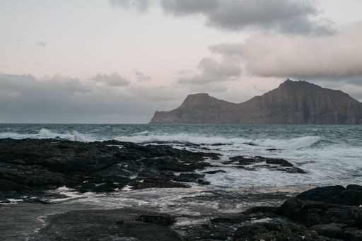 An idyllic seascape featuring a tranquil turquoise ocean gently rolling up onto a beach of white sand, with a rocky island in the background