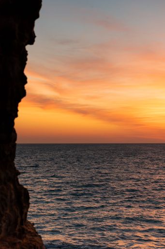 A stunning sunset over the ocean is captured from behind a rocky cliffside