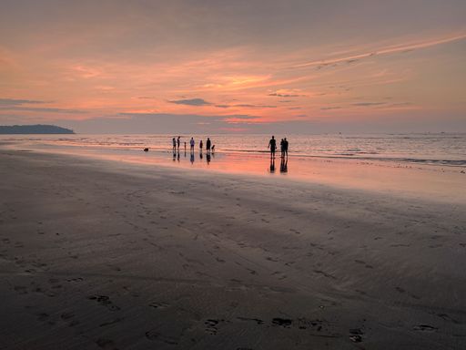 A group of people walking together on a sandy beach at sunset, with the ocean in the backdrop