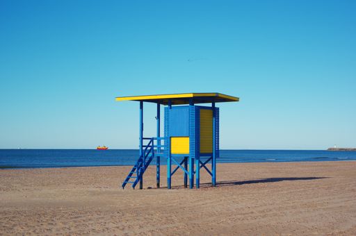 A blue and yellow lifeguard tower on the beach under the clear blue sky