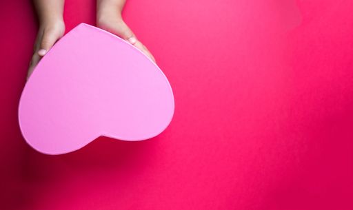 The hands holding a heart-shaped gift isolated on a red background with free space for text- mother's day concept