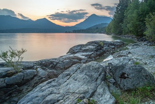 A scenic lake surrounded by majestic mountains, lush green grass, and large granite rocks