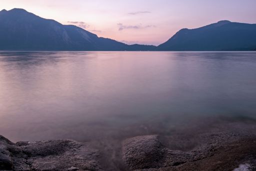 A picturesque landscape featuring a sunset over majestic mountain peaks situated near a tranquil ocean shore