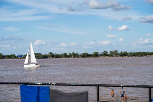 Sailboat navigating the Parana river in front of the island and people in the river on a sunny and clear day