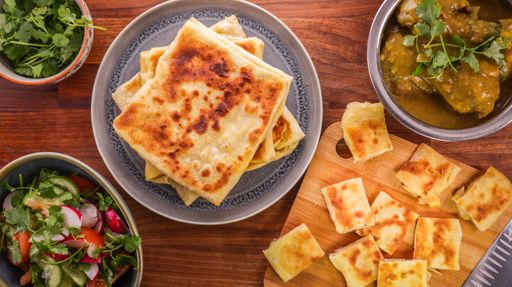 An overhead shot of sliced roti, curry, and salad  on a wooden table