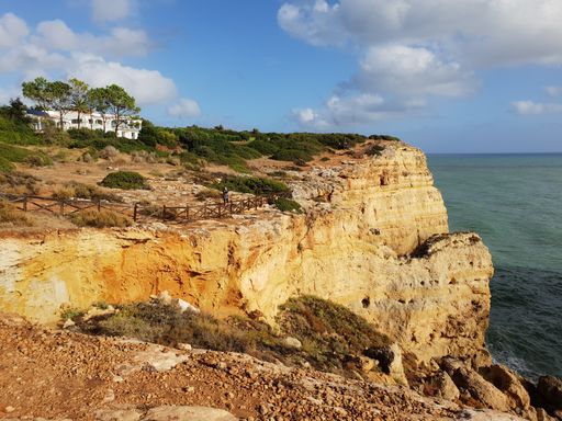 coastline by the sea in Portugal with a white house in the distance with yellow rocks and blue part cloudy sky. Praia da Marinha