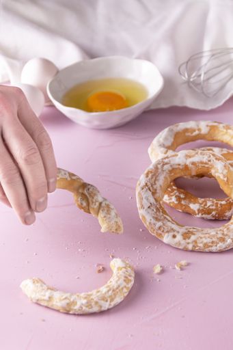A hand picking glazed bagels with eggs, egg beater, napkin on a pink surface