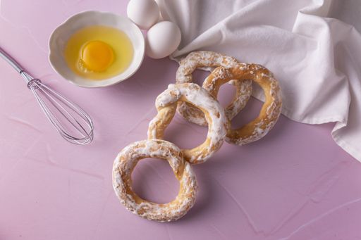 A high anglshot of glazed bagels with eggs, egg beater, napkin on a pink surface