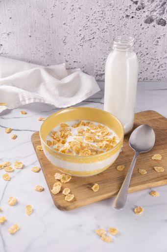 A vertical shot of cereal bowl with milk and spoon on a wooden chopping board