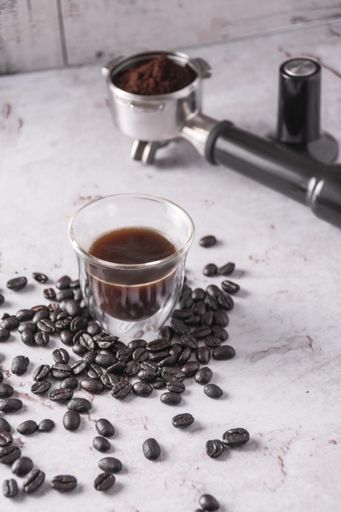 A vertical shot of black coffee, coffee beans, and portafilter on a marble surface